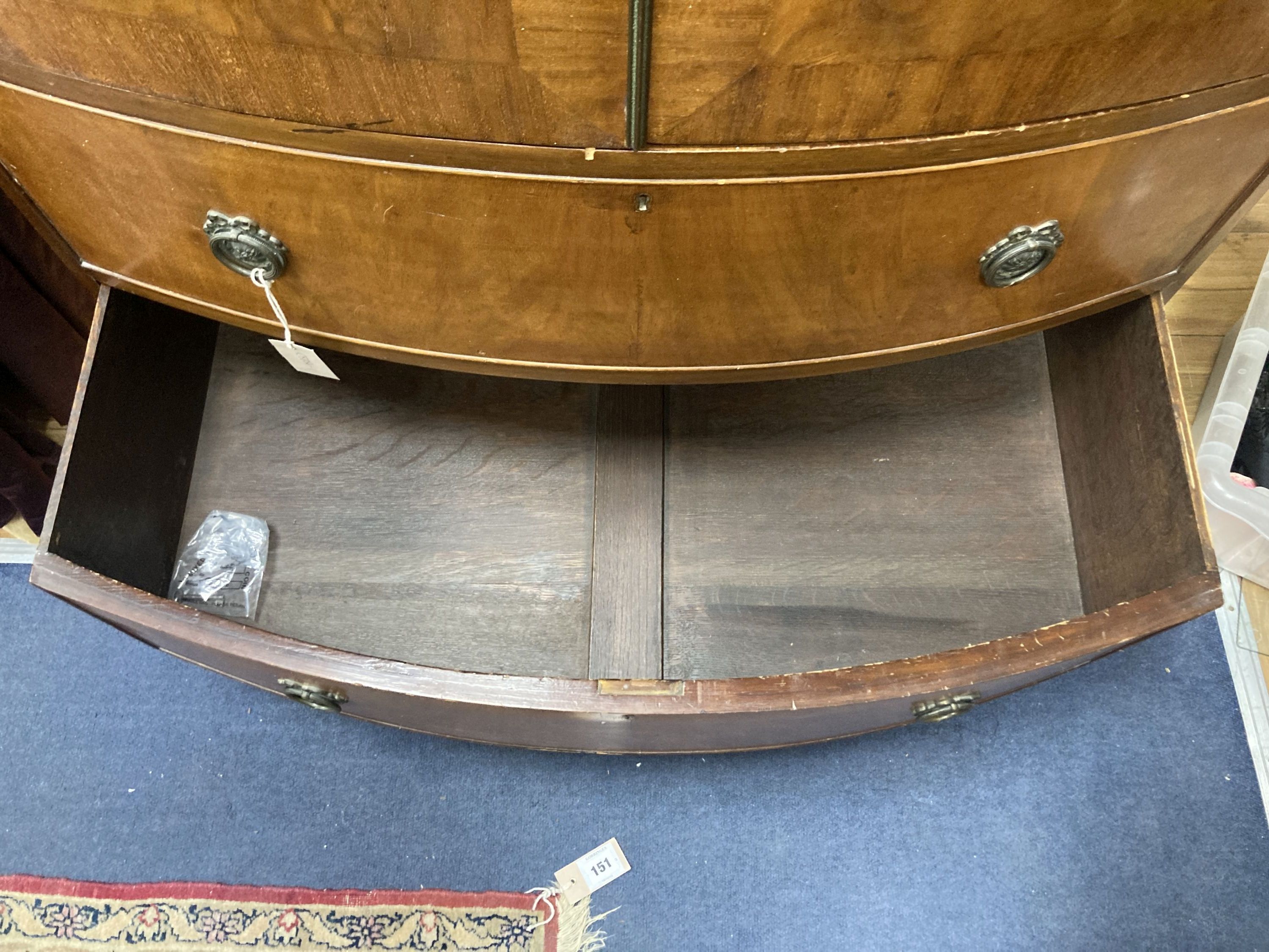 A small early 20th century bow fronted wardrobe, the Greek key frieze above flame veneered and cross banded panelled doors, over two lo